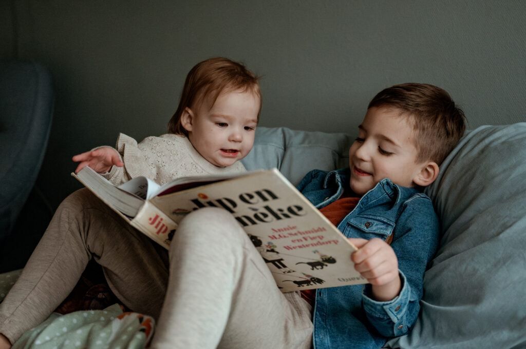 Herinneringen vastleggen. Oudere broer leest een boek voor aan zijn kleine zusje op bed.