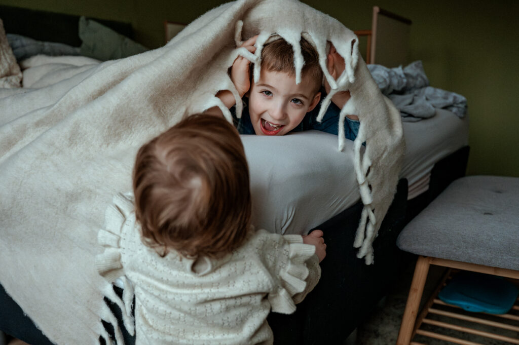 Herinneringen vastleggen. Jongen verstopt zich onder de dekens terwijl zijn kleine zus hem zoekt.