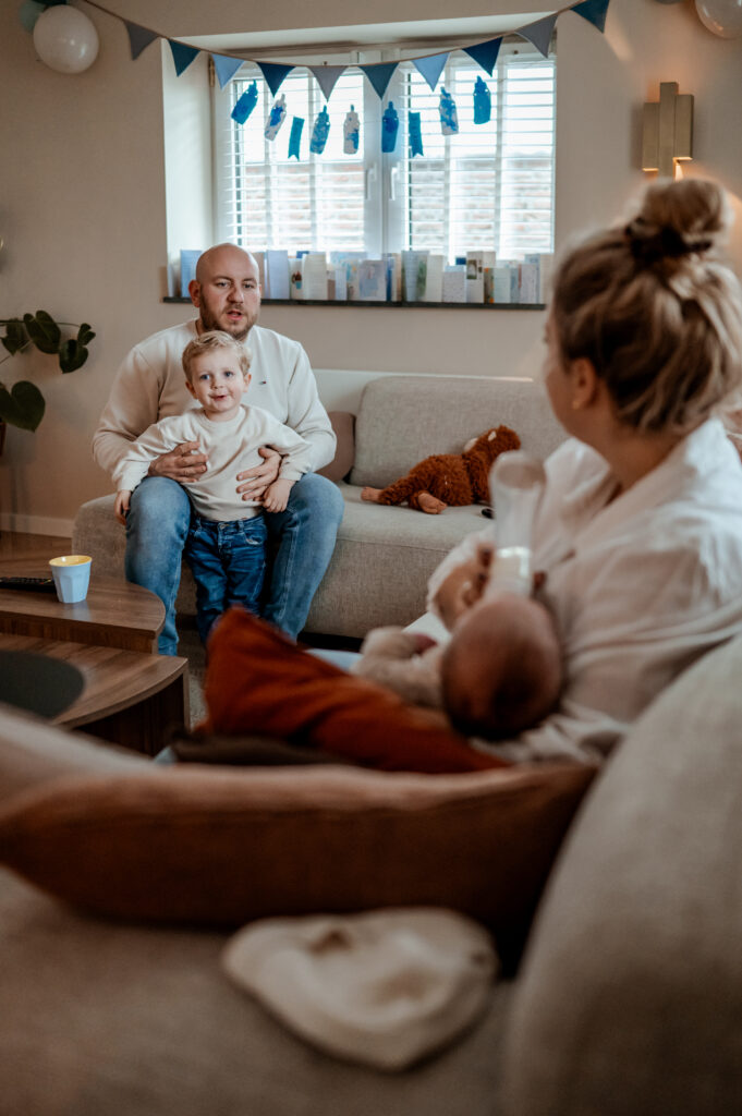 Newbornshoot aan huis. Moeder voedt de baby en vader speelt met de grote broer