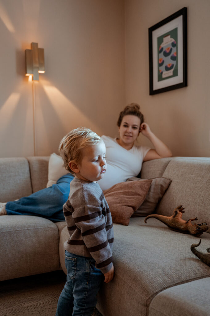 Zwangere moeder kijkt toe hoe haar zoon speelt met de dino's tijdens een fotoshoot aan huis