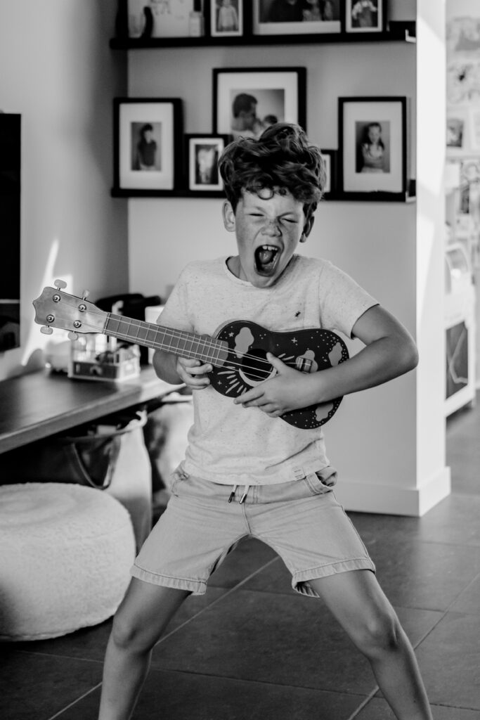 Zwart wit portret van een jongen die lekker thuis aan het spelen is met zijn gitaar tijdens een shoot met Sanne Creuels Photography