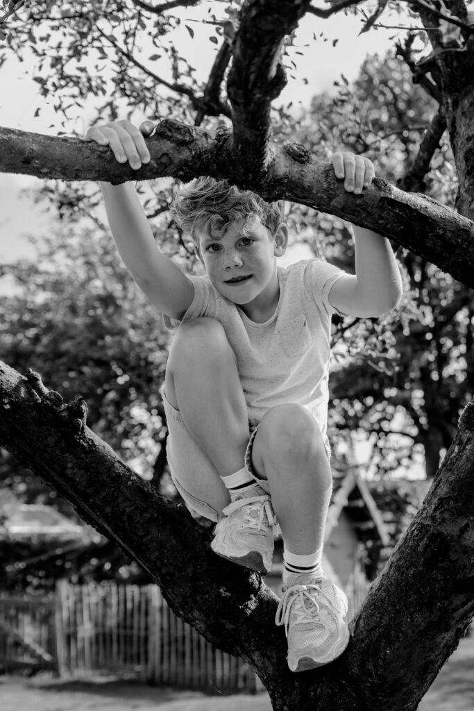 Zwart wit portret van een jongen die in de boom klimt tijdens een shoot met Sanne Creuels Photography