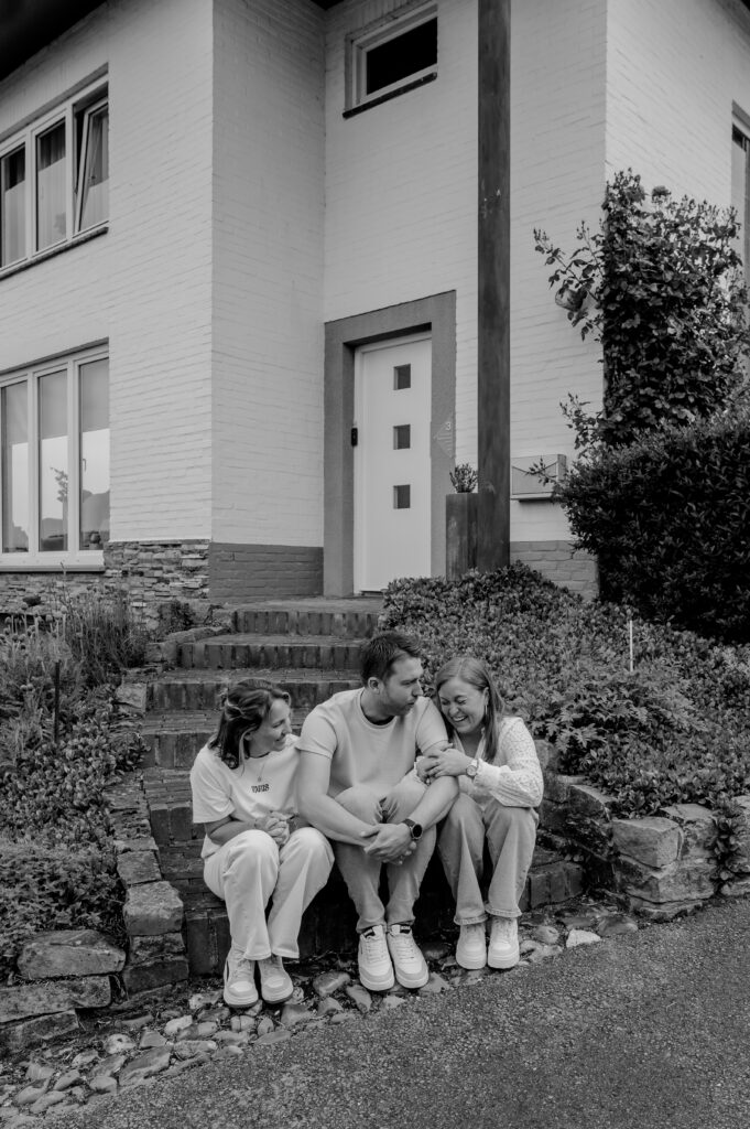 Sanne Creuëls Photography - zwart wit foto van drie volwassen kinderen voor hun ouderlijk huis tijdens hun familieshoot in Zuid-Limburg